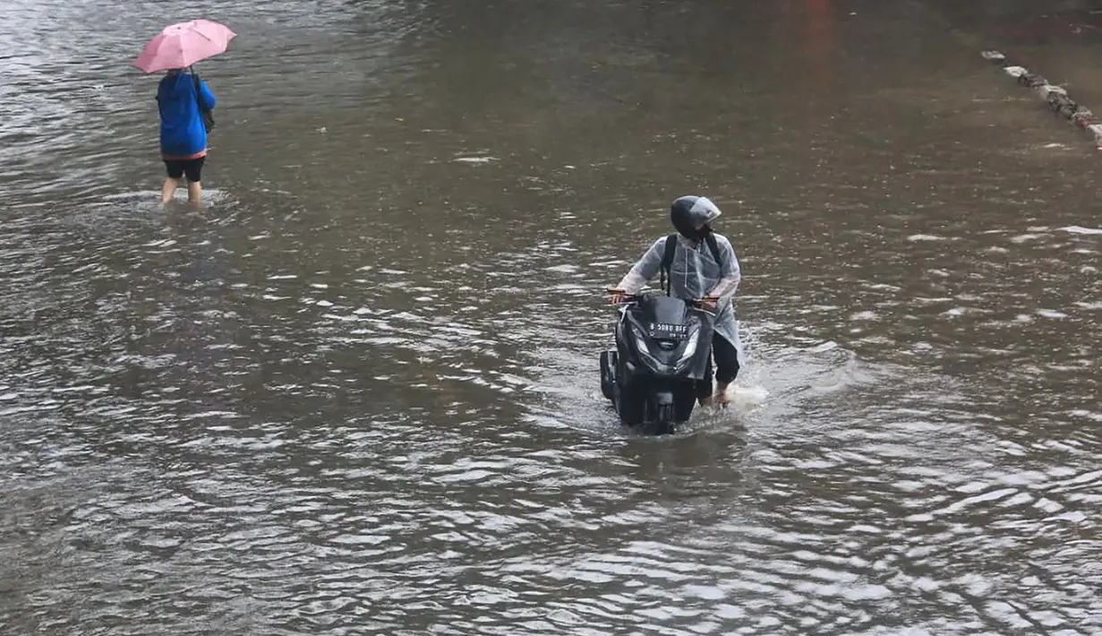 Ketinggian air yang menggenangi permukiman dan jalan bervariasi, mulai dari sekitar 20 sentimeter hingga mencapai hampir satu meter di titik-titik tertentu. Tampak dalam foto, pengendara dan pejalan kaki melintasi banjir yang menggenangi Jalan Jembatan Tiga Raya, Jakarta Utara, Senin (12/1/2026). (merdeka.com/Arie Basuki)