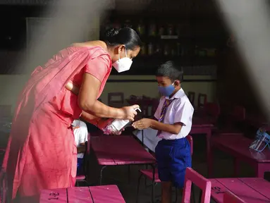 Seorang guru menyemprotkan disinfektan ke telapak tangan siswa sekolah dasar pada awal pelajaran di sebuah sekolah di Kolombo, Sri Lanka, 25 Oktober 2021. Sri Lanka memulai kembali semua sekolah dasar yang telah ditutup lebih dari enam bulan karena pandemi COVID-19. (AP Photo/Eranga Jayawardena)