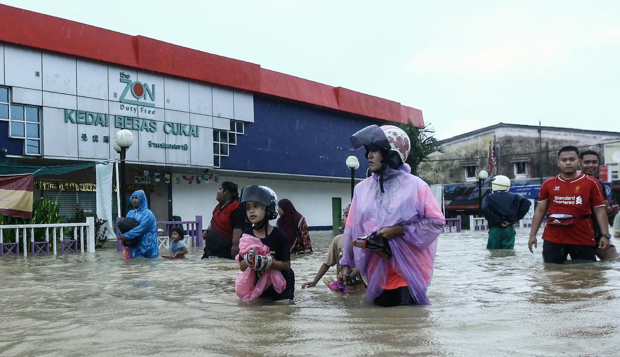 Seorang wanita bersama anaknya melintas di depan sebuah toko yang terendam banjir di Rantau Panjang, Selasa (3/1). Akibat hujan lebat yang turun terus menerus selama empat hari di Malaysia, 5.000 warga terpaksa dievakuasi. (AFP PHOTO/STR/Malaysia OUT)