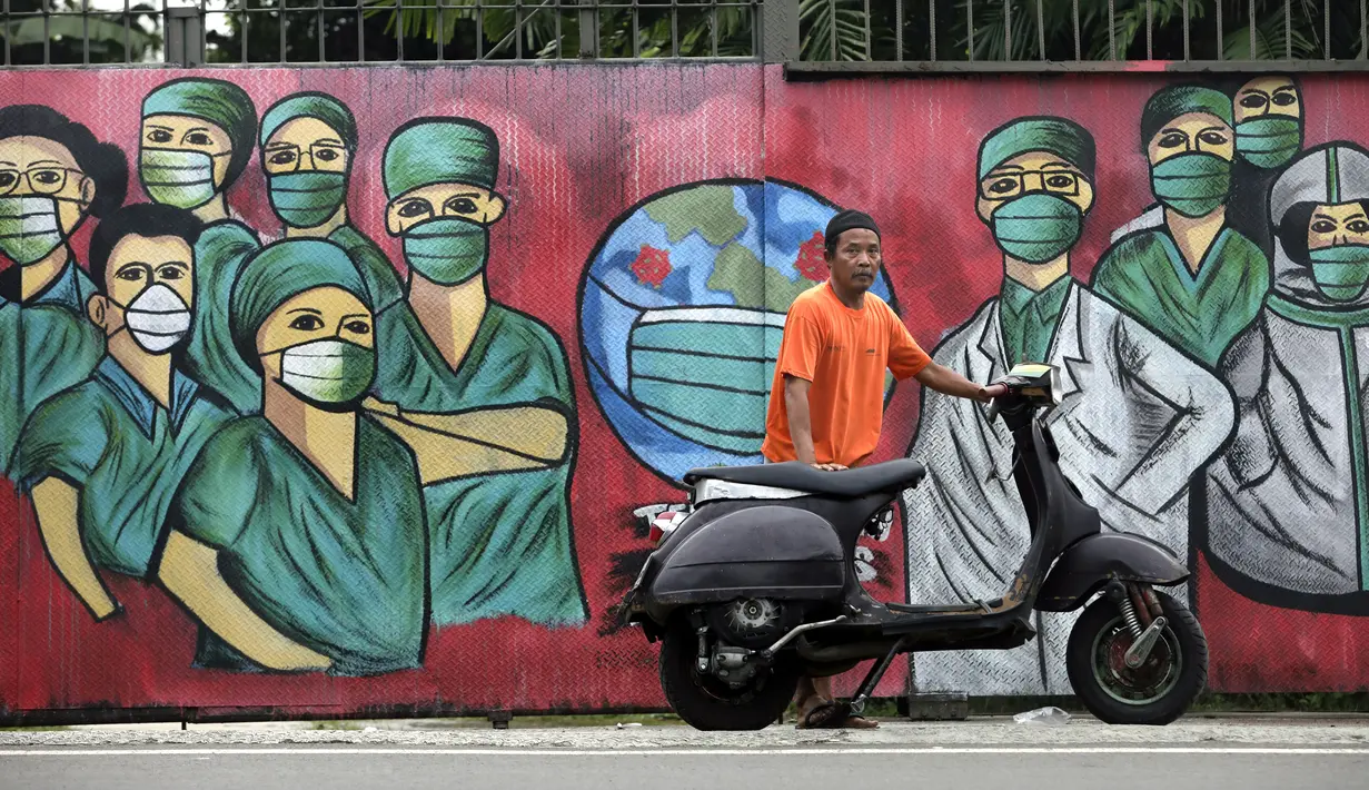 Seorang pengendara sepeda motor berhenti dekat mural yang dibuat sebagai penghormatan terhadap petugas medis yang sedang melawan virus corona COVID-19 di Depok, Jawa Barat, Indonesia, Rabu (15/4/2020). (AP Photo/Dita Alangkara)