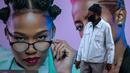 Seorang pria yang mengenakan masker berdiri di depan papan iklan produk rambut di Soweto, Afrika Selatan, Senin (29/6/2020). (AP Photo/Themba Hadebe)