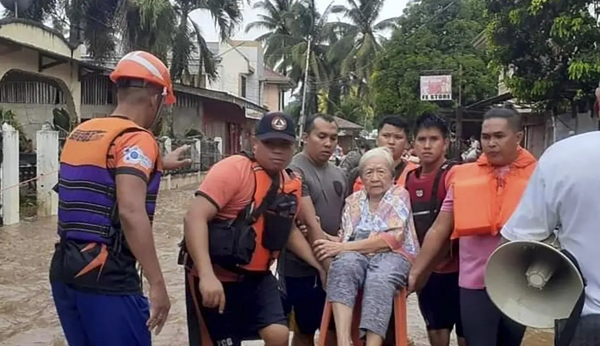 Seorang wanita tua duduk di kursi sambil digendong oleh personel penjaga pantai yang mengarungi banjir di Plaridel, provinsi Misamis Occidental di Filipina selatan, Senin, 26 Desember 2022. Hujan lebat dan banjir menghancurkan beberapa bagian Filipina. (Philippine Coast Guard via AP)