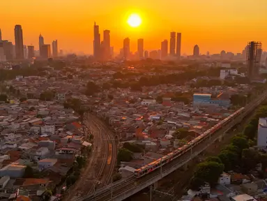 Rangkaian kereta melewati kawasan padat penduduk dengan latar belakang gedung bertingkat saat matahari terbenam di kawasan Manggarai, Jakarta, Kamis, 16/07/ 2026. (KLY/ Arie Basuki)