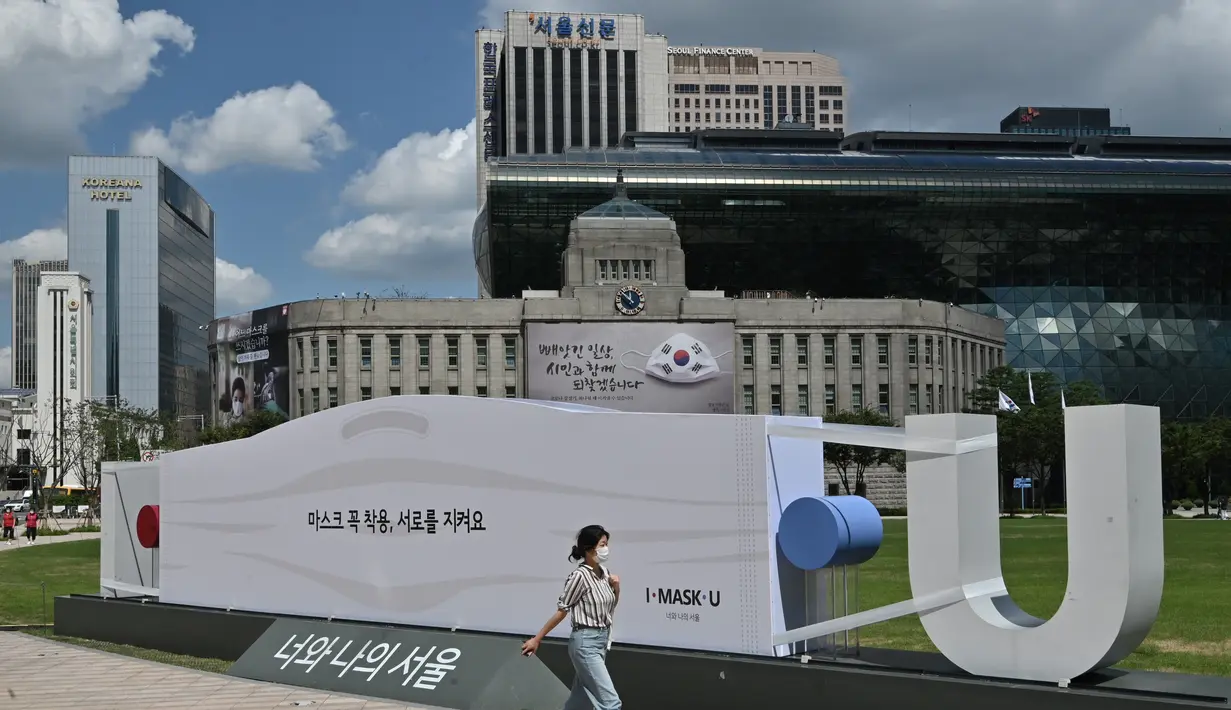 Seorang wanita berjalan melewati patung berbentuk topeng di depan Balai Kota Seoul di Seoul (4/9/2020). Korea Selatan melaporkan 198 kasus Covid-19 baru pada 4 September, hari ke-22 berturut-turut meningkat tiga digit. (AFP/Jung Yeon-je)
