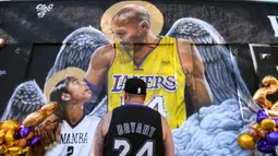 Seorang fans berdiri di depan lukisan mural bintang LA Lakers, Kobe Bryant bersama putrinya, Gianna di Los Angeles, California, Selasa (26/1/2021). Lukisan dibuat untuk mengenang 1 tahun tragedi kecelakaan helikopter yang menewaskan keduanya. (Getty Images via AFP/Harry How)