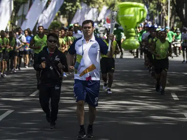 Pevoli legendaris Indonesia, Pascal Wilmar, berlari membawa obor Asian Games XVIII saat pawai di Denpasar, Bali, Selasa (24/7/2018). Sebanyak 53 kota di Indonesia akan dilalui oleh obor Asian Games. (Bola.com/Vitalis Yogi Trisna)