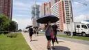 Orang-orang berlindung di bawah payung saat mereka berjalan di sepanjang Mirae Street selama suhu 34 derajat celsius, di Pyongyang, Korea Utara, Rabu (21/7/2021). Musim Panas dimulai pada bulan Juni hingga Agustus, dan puncak musim panas adalah bulan Agustus. (KIM Won Jin / AFP)