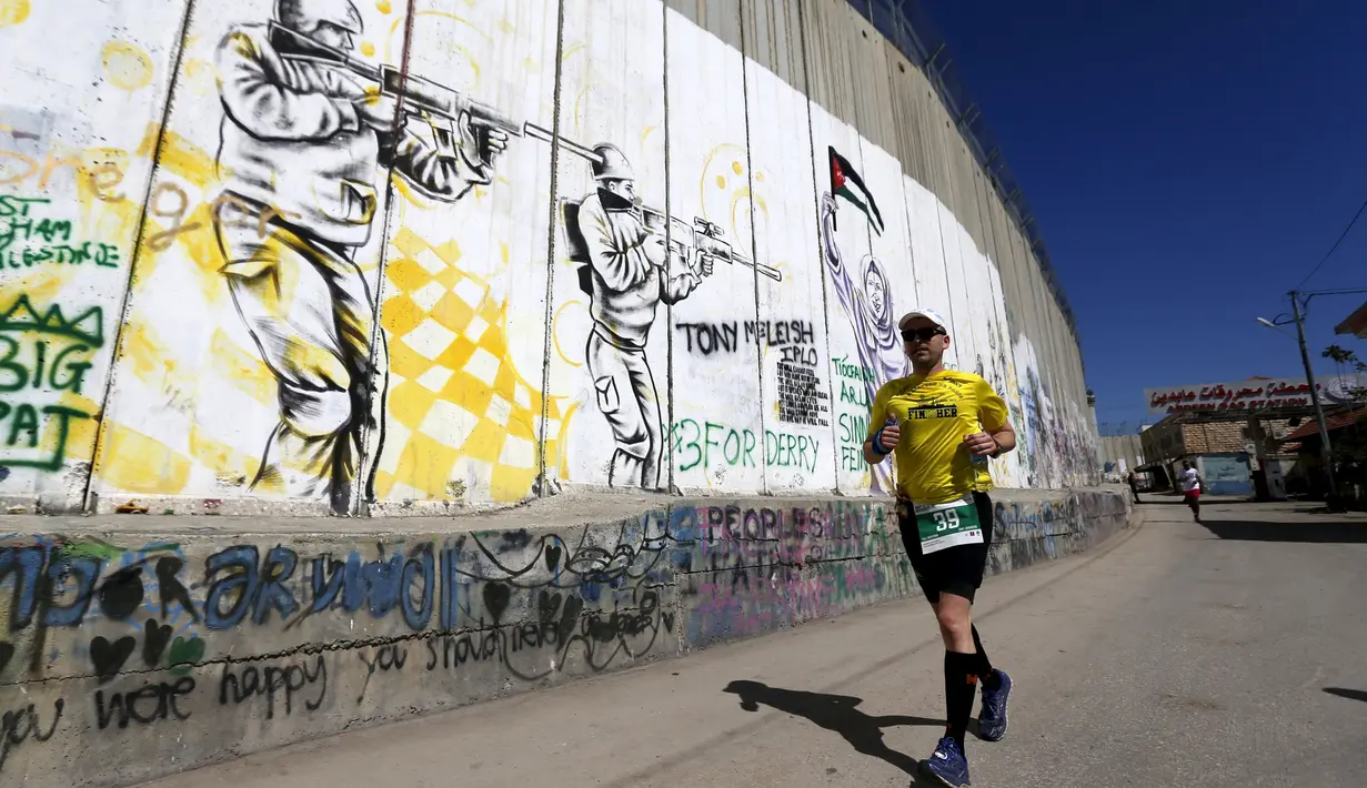 Peserta berlari menyusuri tembok pemisah Israel selama Right to Movement Maraton di kota Bethlehem, Palestina, Jumat (1/4). Tembok ini menjadi sarana bagi seniman jalanan untuk menuangkan keahliannya. (REUTERS / Ammar Awad)