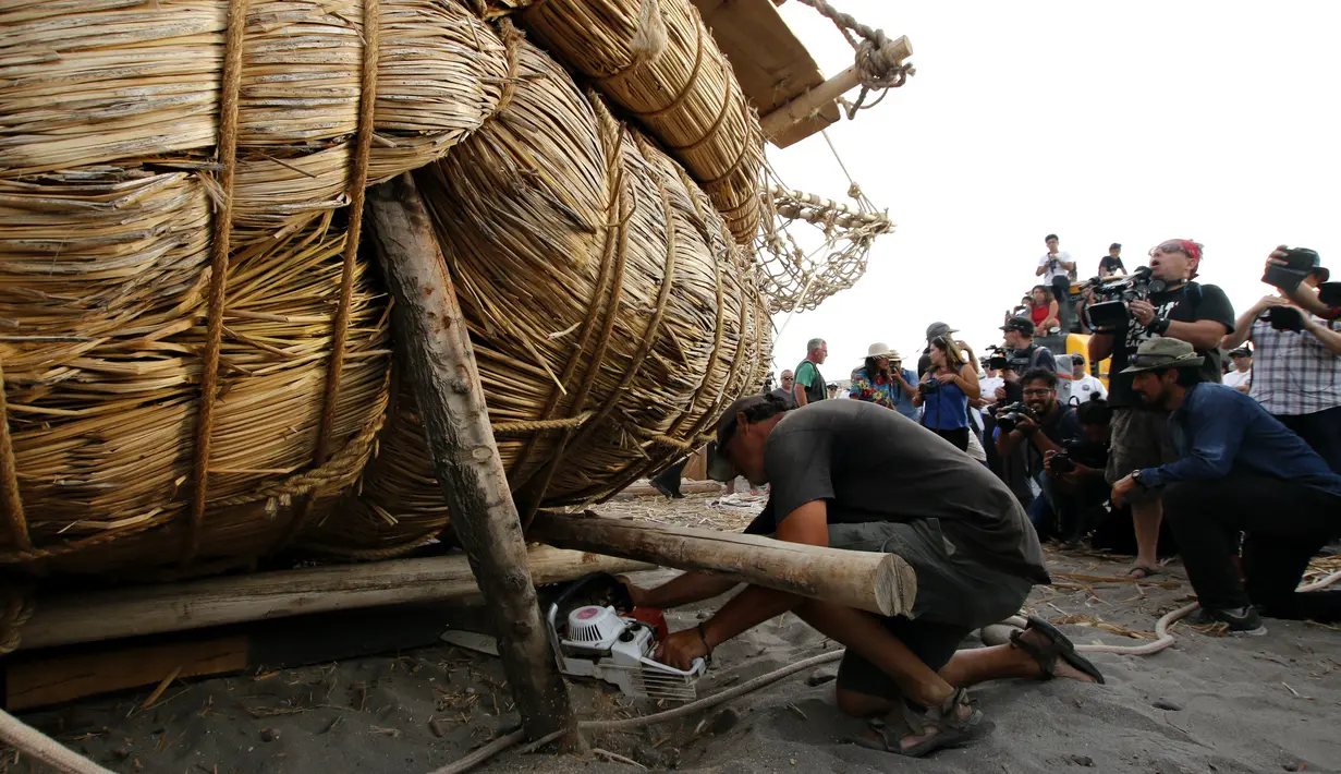 Seorang kru memperbaiki perahu Viracocha III yang rusak sebelum berlayar kembali ke laut lepas di Pantai Chinchorro di kota Arica, Chili (5/2). Perahu yang terbuat dengan cara tradisional ini akan berlayar ke Australia. (AFP Photo/Ignacio Munoz)