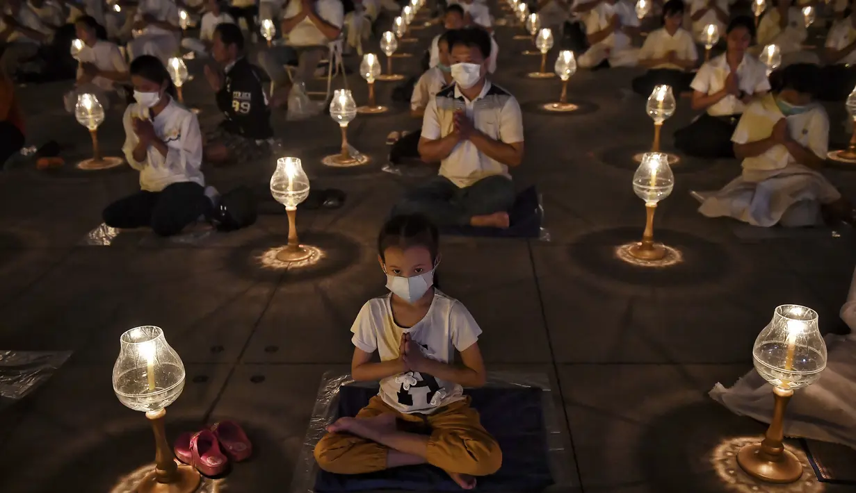 Umat Buddha mengenakan masker saat berdoa bersama setelah pemerintah Thailand mengumumkan 14 orang terkonfirmasi infeksi virus corona di kuil Buddha Wat Dhammakaya, Bangkok (31/1/2020). (AFP Photo/Lillian Suwanrumpha)