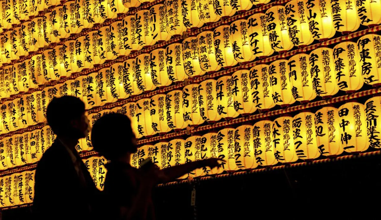 Para pengunjung melihat lentera kertas saat Festival Mitama di Kuil Yasukuni, Tokyo, Jepang, Rabu (14/7/2021). Festival Mitama dirayakan sejak 1947 untuk menghormati jiwa para arwah yang diabadikan serta tentara yang gugur dari perang Jepang di masa lalu. (BEHROUZ MEHRI/AFP)
