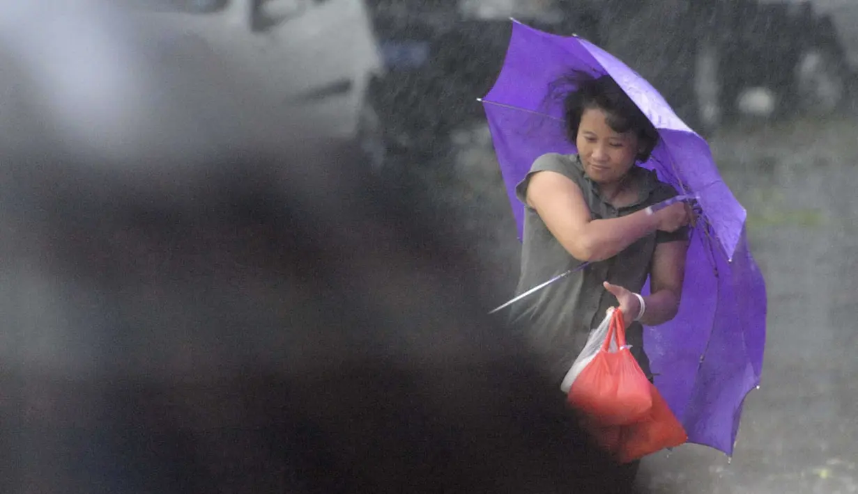 Seorang wanita memegang payung saat berjalan di tengah hembusan Topan Kalmaegi yang menerjang wilayah Qionghai di provinsi Hainan, Tiongkok, (16/9/2014). (REUTERS/Stringer)