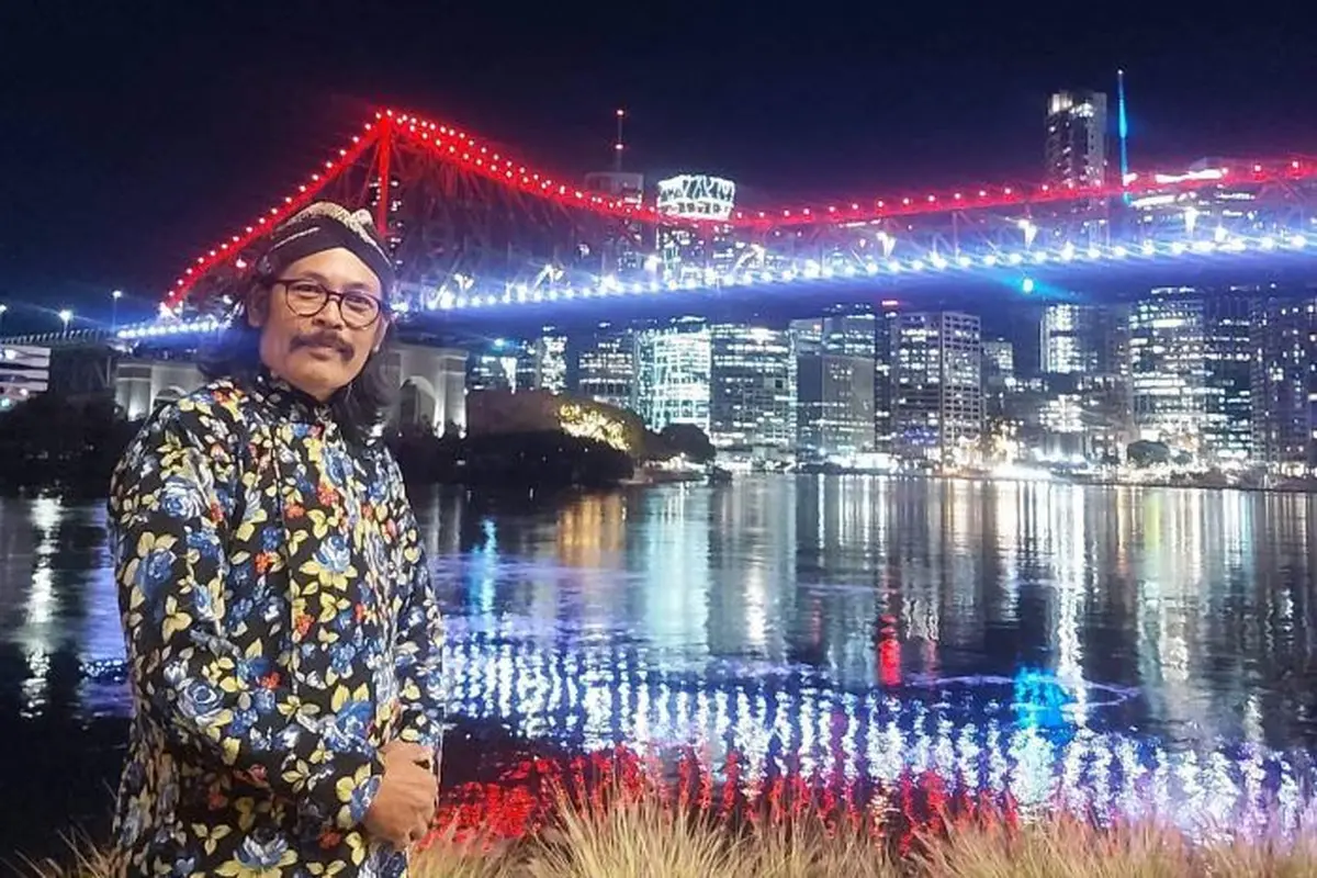 Yogi menggunakan baju khas Jawa pada Senin malam sambil mengabadikan momen bersejarah dengan jembatan Brisbane yang berwarna merah putih. (Facebook. Agustinus Jogiono)
