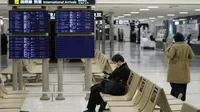 Penumpang duduk dekat layar informasi kedatangan penerbangan internasional di Bandara Narita, Tokyo, Kamis (2/12/2021). Maskapai-maskapai internasional diminta menangguhkan reservasi baru pada semua penerbangan masuk ke Jepang hingga akhir Desember terkait varian Omicron. (AP Photo/Hiro Komae)