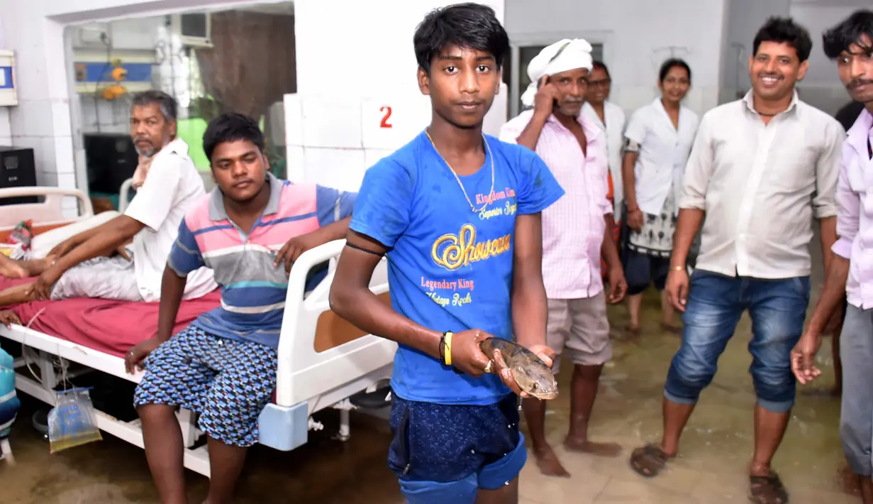 Anggota keluarga pasien yang dirawat, menangkap seekor ikan di dalam bangsal rumah sakit kamar yang tergenang banjir di Nalanda Medical College Hospital, daerah Bihar, India, 29 Juli 2018. Peristiwa unik ini ramai menjadi perbincangan netizen. (AFP PHOTO)