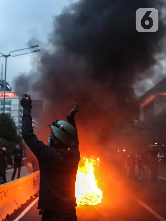 Massa aksi demo menolak Omnibus Law UU Cipta Kerja membakar ban bekas di Jalan Medan Merdeka Barat, Jakarta Pusat, Selasa (20/10/2020). Gelombang protes tolak UU Cipta Kerja belum surut sejak disahkan pada 5 Oktober lalu. (Liputan6.com/Johan Tallo)