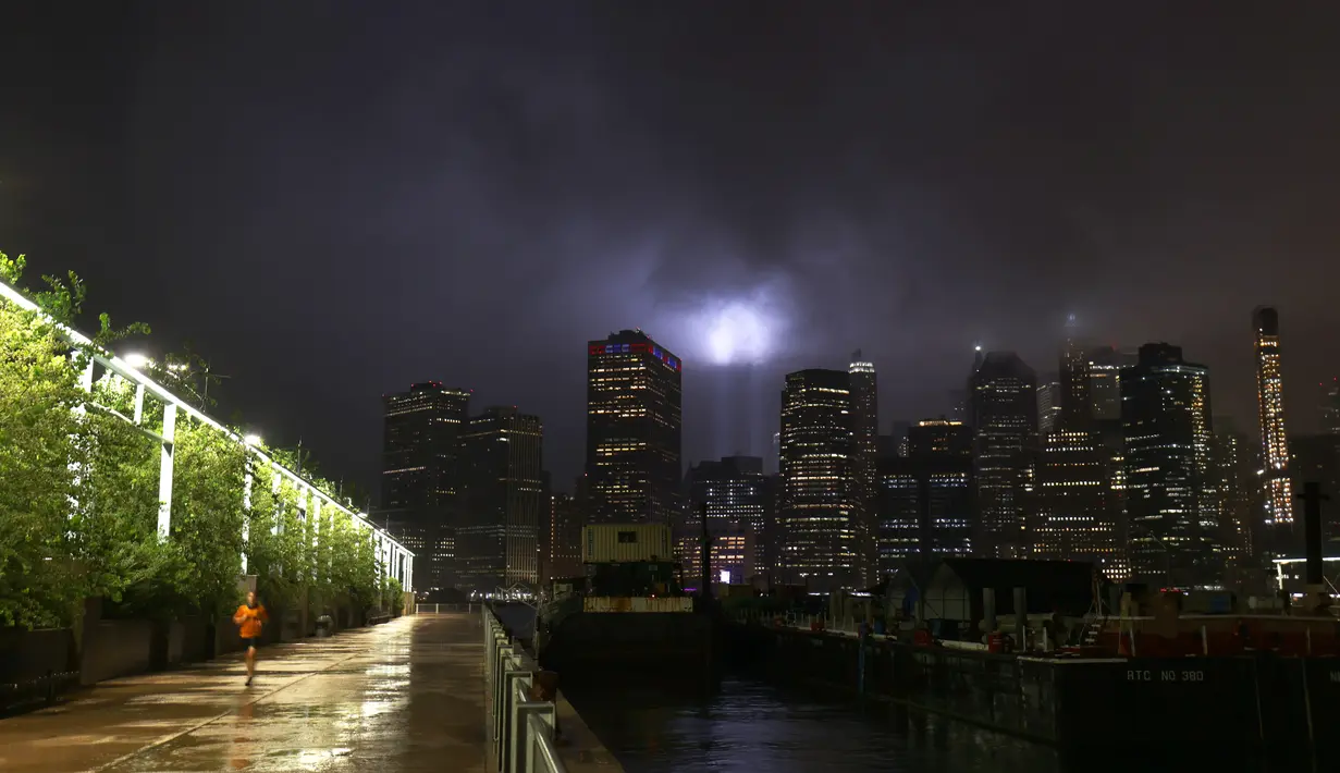 Seorang pria berlari di Brooklyn Bridge Park saat penghormatan 9/11 dalam Cahaya bersinar di langit Manhattan di New York City (10/9/2020). Tribute in Light tahunan National September 11 Memorial & Museum awalnya dibatalkan tahun ini karena pandemi COVID-19. (Michael M. Santiago/Getty Images/AFP)