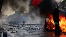 Seorang demonstran mengibarkan bendera Albania di depan mobil yang terbakar saat aksi unjuk rasa antipemerintah di luar kantor Perdana Menteri di Tirana, Albania, Sabtu (17/10/2026). (AP Photo/Hameraldi Agolli)