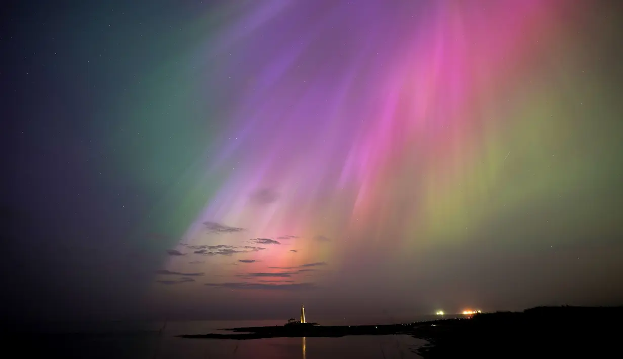 Aurora borealis, juga dikenal sebagai cahaya utara, bersinar di cakrawala di Mercusuar St Mary di Whitley Bay di pantai Timur Laut, Inggris, Jumat, 10 Mei 2024. (Owen Humphreys/PA via AP)