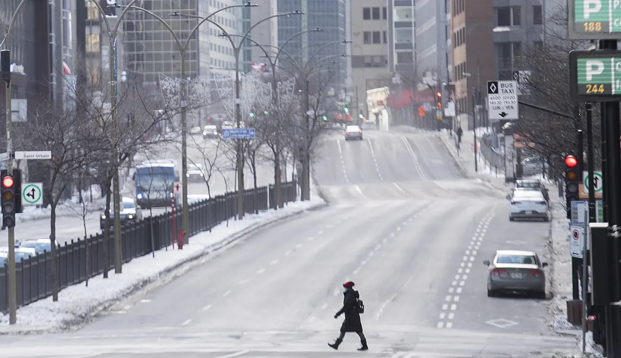 Seorang perempuan mengenakan masker saat melintasi jalan raya Rene-Levesque di Montreal, Kanada, Minggu (10/1/2021). Pemerintah Quebec memberlakukan lockdown dan jam malam untuk membantu menghentikan penyebaran COVID-19 yang berlangsung hingga 8 Februari. (Graham Hughes/The Canadian Press via AP)