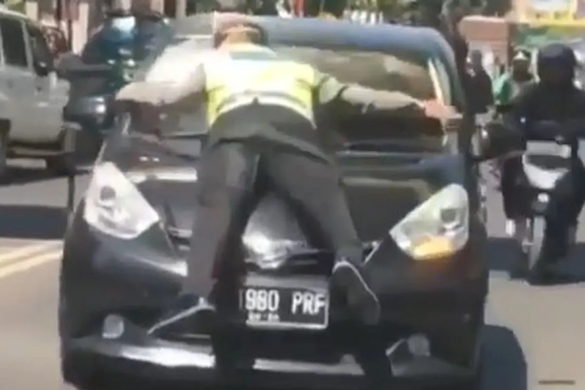 Terlihat jelas polisi tersebut berpegang pada kedua mobil saat kendaraan melaju dengan kecepatan sedang.