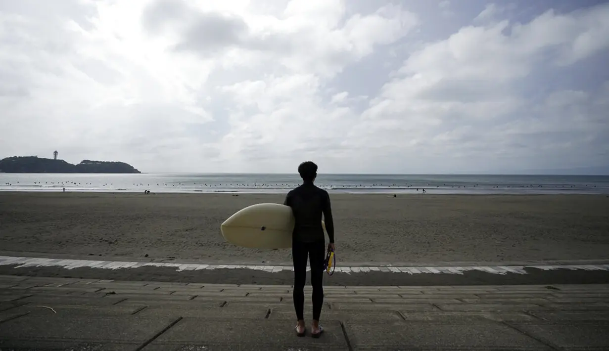 Seorang peselancar melihat pantai Katase-kaigan yang berangin, Fujisawa, Prefektur Kanagawa, selatan Tokyo, Jepang, Kamis (24/9/2020). Badai Tropis Dolphin bergerak di sepanjang pantai Pasifik Jepang. (AP Photo/Eugene Hoshiko)