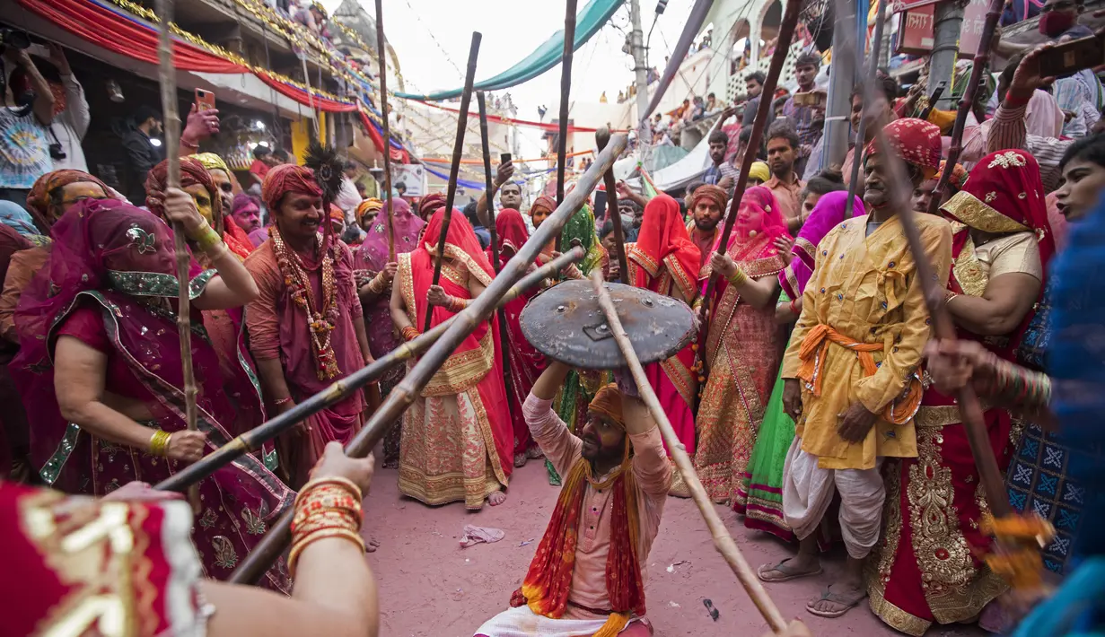Perempuan Hindu memukuli seorang pria dengan tongkat saat mereka secara tradisional merayakan Lathmar Holi di dekat sebuah di Barsana, India, Selasa (23/3/2021). Para pria biasanya membawa perisai untuk melindungi diri mereka sementara wanita memukuli mereka dengan tongkat. (Xavier GALIANA/AFP)