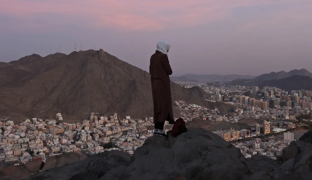 Seorang peziarah muslim melihat Kota Suci Mekkah dari atas Jabal al-Noor atau Gunung Cahaya, Arab Saudi, 5 Juli 2022. Satu juta orang, termasuk 850 ribu dari luar negeri, diizinkan untuk berpartisipasi dalam haji tahun ini setelah dua tahun terakhir jumlahnya dikurangi secara drastis karena pandemi virus corona COVID-19. (Christina ASSI/AFP)