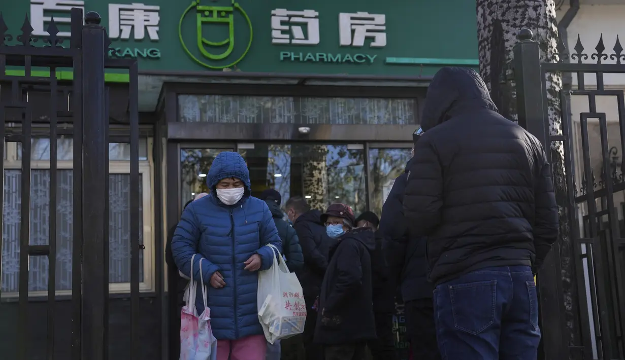 Seorang perempuan membawa sekantong obat flu dan demam saat warga antre untuk mendapatkan obat di apotek di Beijing, Minggu (11/12/2022).  China mengerahkan lebih banyak fasilitas perawatan intensif dan memperkuat layanan rumah sakitnya ketika menghadapi lonjakan kasus Covid-19. (AP Photo/Andy Wong)