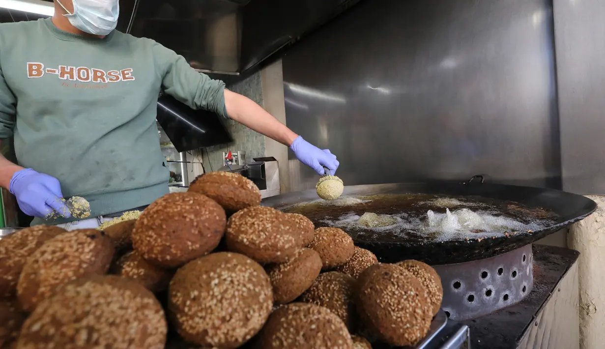 Juru masak Palestina mengenakan sarung tangan dan masker saat menggoreng falafel di sebuah restoran lokal di kota Hebron, Tepi Barat yang diduduki pada 29 April  2020. Pada bulan suci Ramadan, falafel sering dimakan sebagai hidangan buka puasa. (HAZEM BADER / AFP)