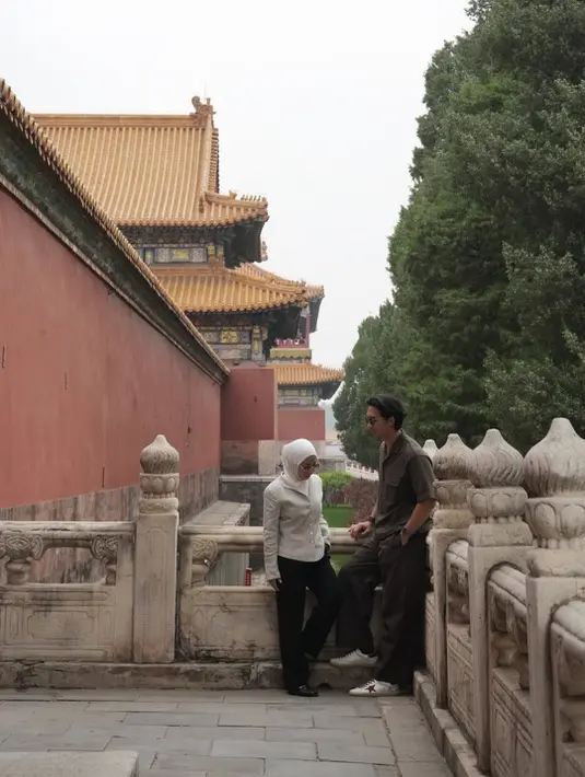 Sementara itu, pada potret lain bersama Indra Priawan di area bangunan berarsitektur tradisional China, Nikita memilih tampilan yang lebih minimalis dalam balutan fitted white top dengan detail kancing dan celana hitam straight cut. Siluet sederhana tersebut justru membuat gayanya terlihat refined dan timeless. Dipadukan dengan hijab putih dan pointed shoes hitam, look ini terasa clean sekaligus modern. [Dok/@nikitawillyofficial94].