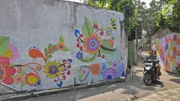 Pengendara motor melintasi gang sempit yang sisi tembok dindingnya dihiasi lukisan mural warna-warni di Kampung Pejaten, Jakarta, Senin (30/4). Mural motif warna-warni itu digagas warga untuk memperindah kampung mereka. (Liputan6.com/Herman Zakharia)