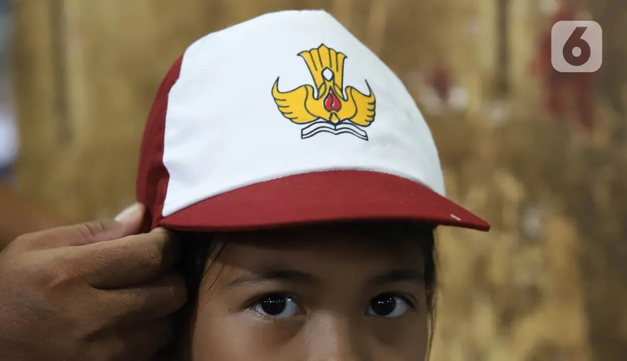 Calon pembeli mencoba topi sekolah kepada anaknya di Pasar Kebayoran Lama, Jakarta, Jumat (8/7/2022). Menjelang dimulainya tahun ajaran baru, para orang tua disibukkan berbelanja baju seragam dan perlengkapan sekolah untuk anak mereka. (Liputan6.com/Angga Yuniar)