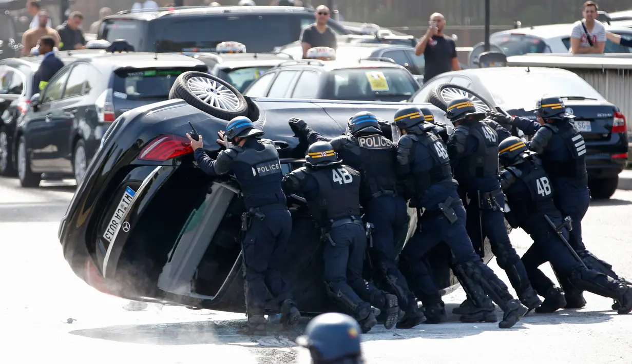Polisi anti huru hara Perancis mendorong mobil terbalik selama protes terhadap mobil mobil layanan Uber, Perancis, Kamis (25/6/2015). Para supir memprotes layanan Online taksi Uber. (REUTERS/Charles Platiau)