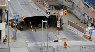 Pekerja mengamati sebuah sinkhole besar yang menganga di Rideau Street, Ottawa, Kanada, Rabu (8/6). Area tersebut berlokasi di daerah yang sedang dilakukan penggalian dan telah ditutup untuk lalu lintas semua kendaraan bermotor. (REUTERS/Chris Wattie)