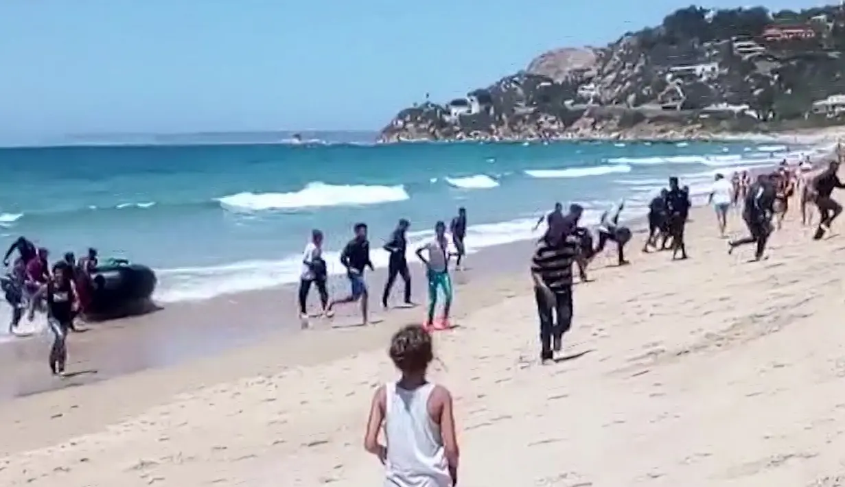Seorang wanita melihat puluhan imigran yang menggunakan perahu karet berlarian menuju pantai Cadiz, Spanyol selatan, 9 Agustus 2017. Para imigran itu langsung berganti pakaian ketika tiba di daratan demi menghindari penangkapan polisi (Carlos Sanz via AP)
