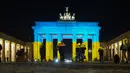 Orang-orang melihat Gerbang Brandenburg yang diterangi dengan warna bendera Ukraina di Berlin, Jerman, Rabu (23/2/2022). Salah satu bangunan ikonik itu diterangi warna bendera nasional Ukraina, biru dan kuning untuk menunjukkan solidaritas selama ketegangan dengan Rusia. (AP Photo/Markus Schreiber)