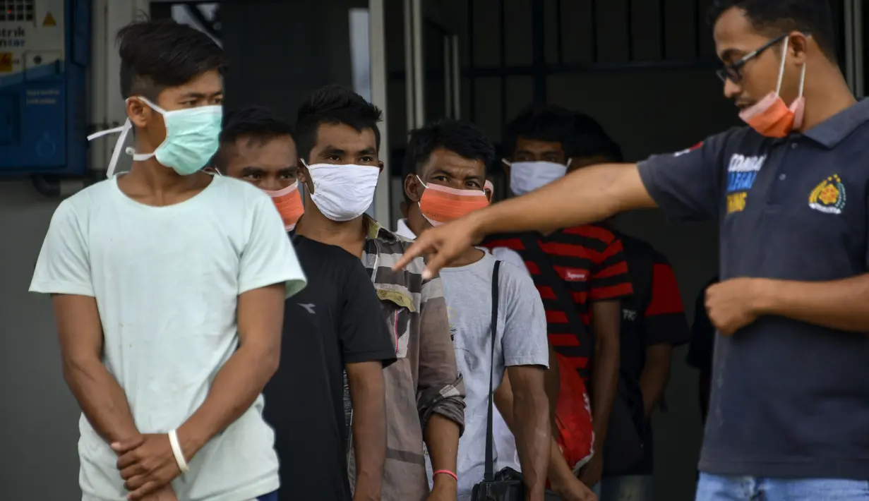 Seorang pejabat Urusan Kelautan dan Perikanan Indonesia (R) berdiri di sebelah nelayan Myanmar yang menunggu untuk dideportasi setelah ditahan selama delapan bulan di Banda Aceh (5/8/2020). (AFP Photo/Chaideer Mahyuddin)