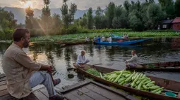 Seorang pria Kashmir menyaksikan orang lain menjual produk mereka di pasar sayur terapung di Danau Dal di Srinagar, Kashmir yang dikuasai India pada 26 Juli 2020. Sayuran yang diperdagangkan di pasar terapung ini disuplai ke Srinagar dan banyak kota di lembah Kashmir. (AP Photo/Dar Yasin)