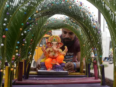 Seorang perajin memajang patung Dewa Ganesha untuk dijual di kios pinggir jalan di Hyderabad, India, Kamis (9/9/2021). Patung dewa Hindu berkepala gajah tersebut banyak dijual jelang Festival Ganesh Chaturthi. (NOAH SEELAM/AFP)