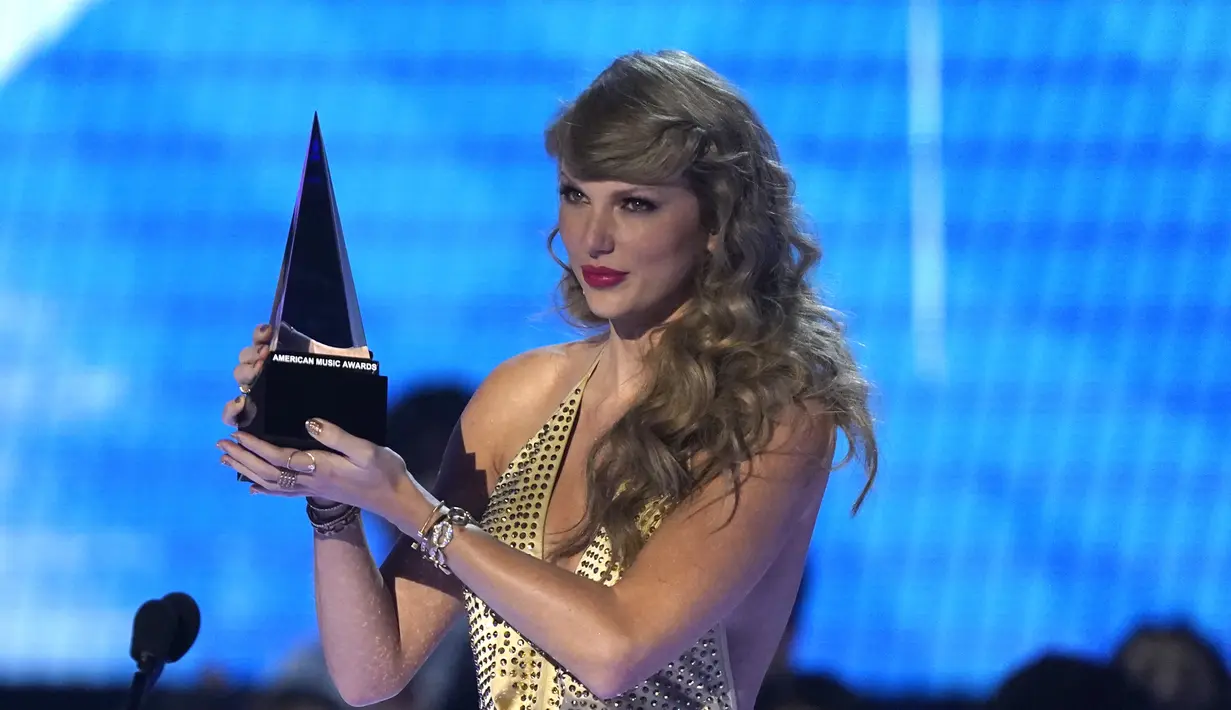 Taylor Swift menerima penghargaan untuk album pop favorit untuk "Red (Taylor's Version)" di American Music Awards di Microsoft Theater di Los Angeles pada Minggu, 20 November 2022. Taylor Swift tampil Ia mengenakan pakaian panjang berwarna gold dengan rambutnya yang panjang bergelombang. (AP Photo/Chris Pizzello)