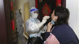 Seorang pekerja medis mengambil sampel swab dari seorang warga selama pemeriksaan Covid-19 dari pintu ke pintu di Kota Zhengzhou, China Tengah, Selasa (1/11/2022). Para pekerja iPhone Apple Inc meninggalkan pabrik karena lokasinya berada dalam zona industri Kota Zhengzhou yang sedang diberlakukan lockdown setelah adanya 64 laporan kasus virus corona di kawasan tersebut. (Chinatopix via AP)