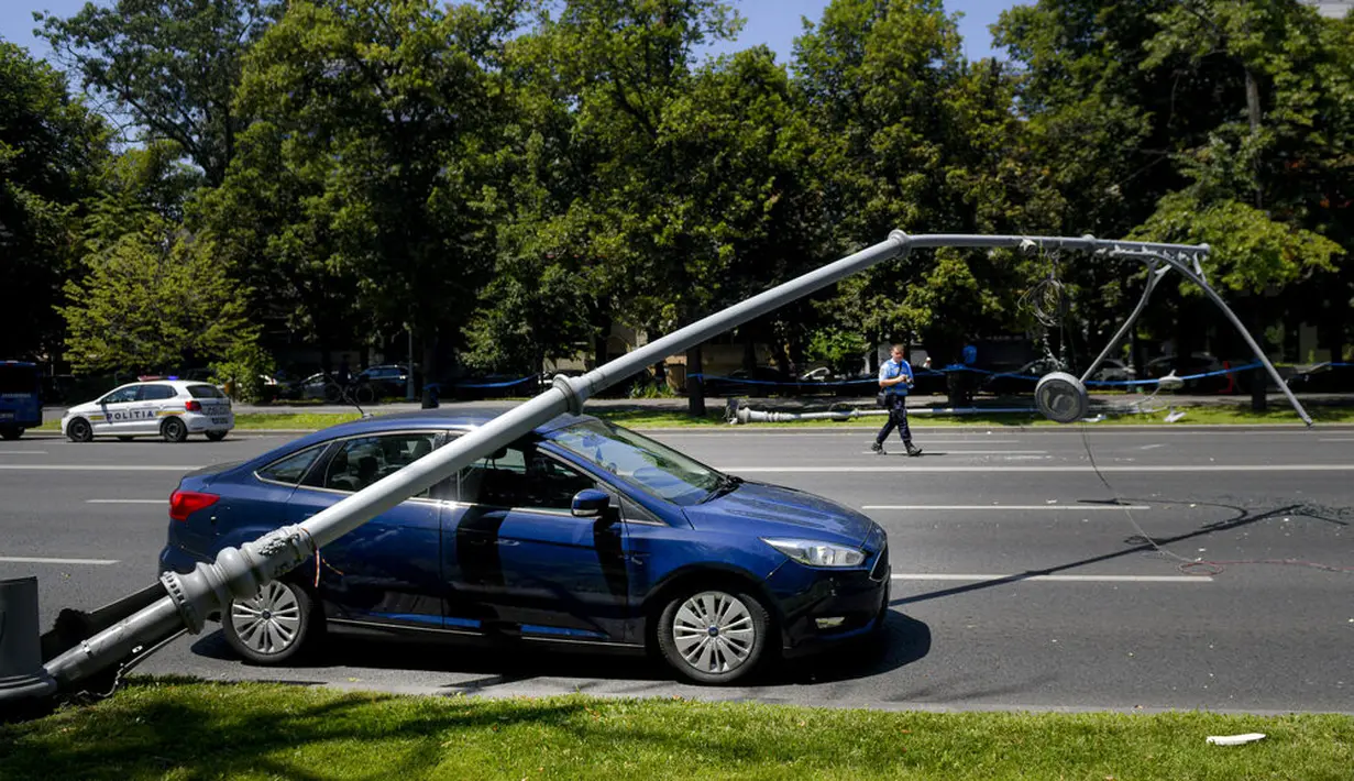 Seorang polisi Rumania mengambil gambar mobil yang rusak setelah tertimpa tiang lampu karena helikopter Black Hawk AS mendarat darurat di boulevard yang sibuk, di Bucharest, Kamis (15/7/2201). Helikopter tersebut mendarat darurat karena masalah teknis. (AP Photo/Andreea Alexandru)