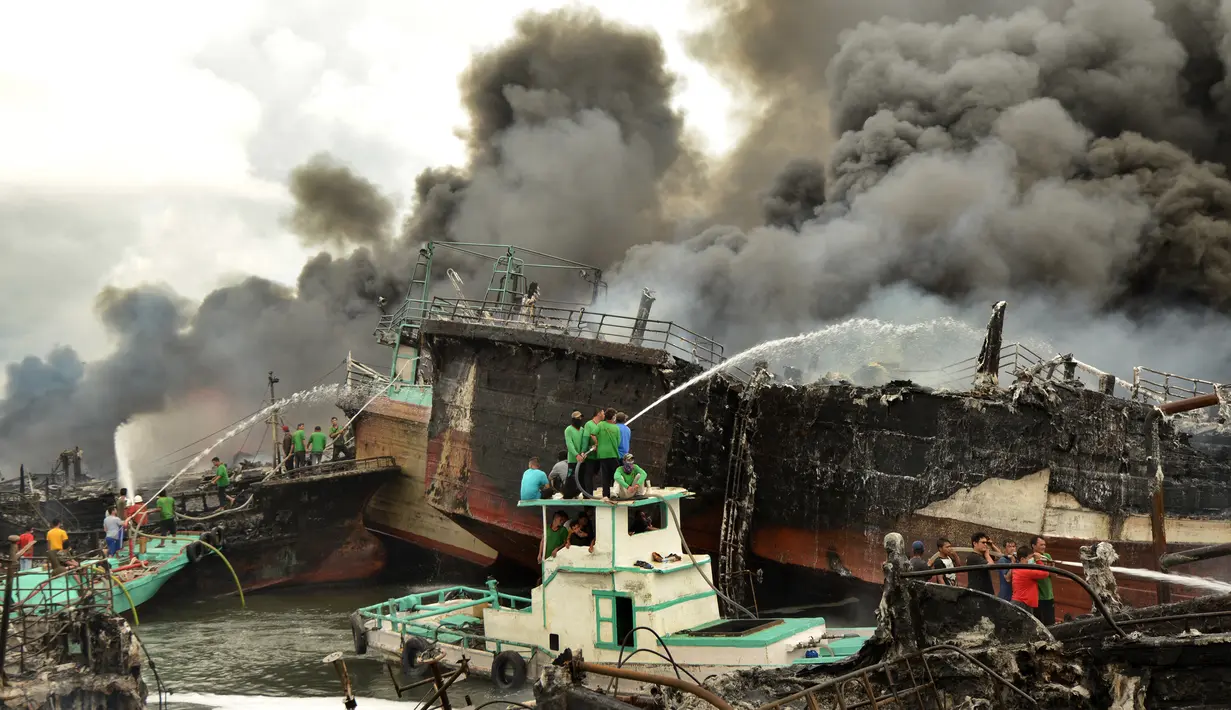 Para pekerja mencoba membantu memadamkan api di kapal nelayan di Pelabuhan Benoa, Denpasar, Bali, Senin (9/7). Kebakaran semakin membesar karena angin cukup kencang. (SONNY TUMBELAKA/AFP)