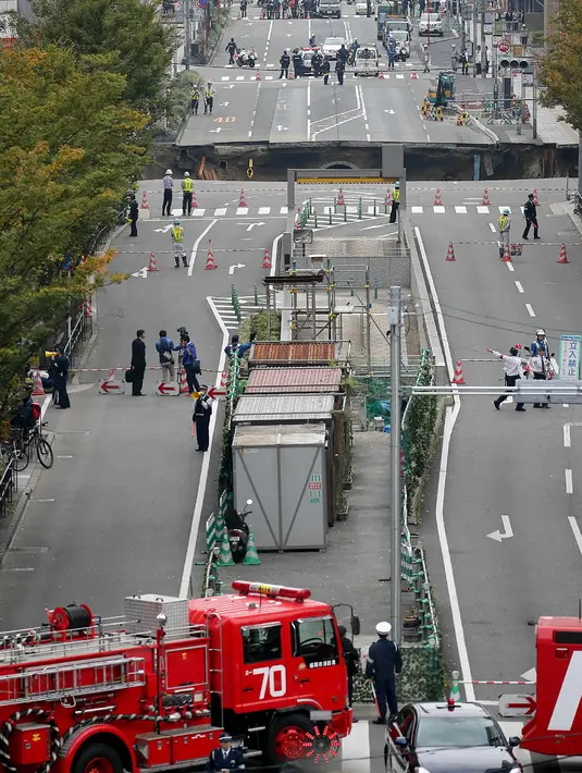 Petugas pemadam dikerahkan ke lokasi munculnya lubang raksasa atau sinkhole di persimpangan dekat Stasiun Hakata, Fukuoka, Jepang, Selasa (8/11). Insiden itu mengakibatkan lalu lintas terputus, pemadaman listrik serta kebocoran gas. (STR/JIJI PRESS/AFP)