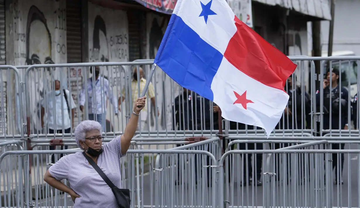 Seorang wanita memegang bendera Panama saat anggota serikat guru yang mogok memprotes selama pawai menuju Majelis Nasional di Panama City, Senin (11/7/2022). Masker tidak lagi diperlukan kecuali di rumah sakit dan transportasi umum. (AP Photo/Arnulfo Franco)