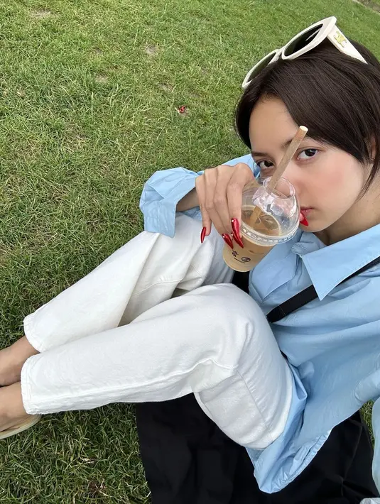 Duduk di atas rumput dengan outfit kasual, Lisa BLACKPINK melakukan selfie menunjukkan es kopinya dan wajah tanpa riasan. Bukankah ia tetap terlihat menawan, Sahabat FIMELA? Foto: Instagram.