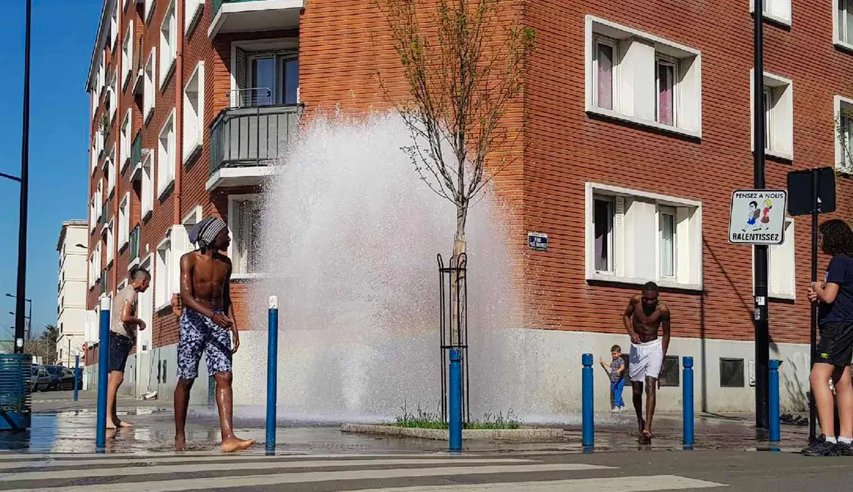 Sejumlah pemuda mendinginkan tubuh di air hidran yang terbuka selama cuaca panas di Aubervilliers, sebelah utara Paris, (19/4). (AFP Photo/Amine Guedaim)