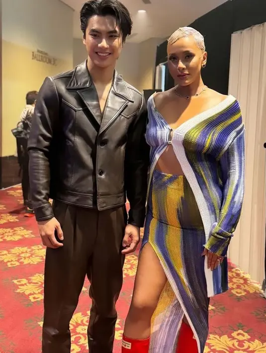 Model dan aktris Kimmy Jayanti yang tampil edgy dengan set cardigan dan high slit skirt motif abstrak, dipadukan boots warna merahnya. Di sampingnya ada aktor Thailand, Ohm Phawat yang tampil gagah dengan jaket kulit hitamnya.  [@kimmyjayanti]
