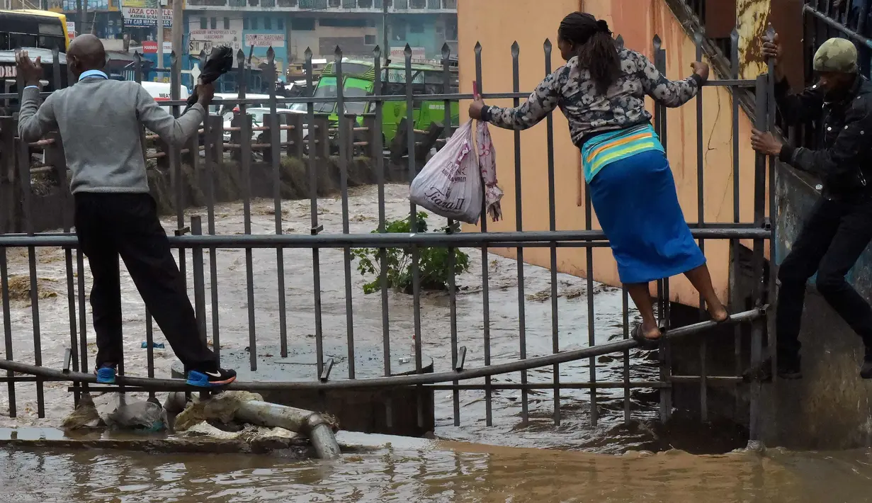 Pejalan kaki berjalan di pagar untuk menyebrang menyusuri jalan yang banjir menuju tempat kerja setelah hujan deras di Nairobi, Kenya (15/3). (AFP Photo/Simon Maina)